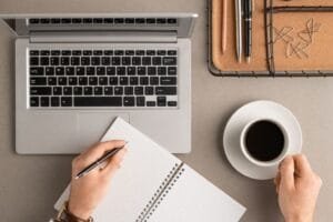 Freelance writer typing on a notebook while using a laptop.